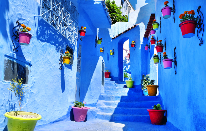 Blaue Gasse mit bunten Blumentöpfen an den Wänden.