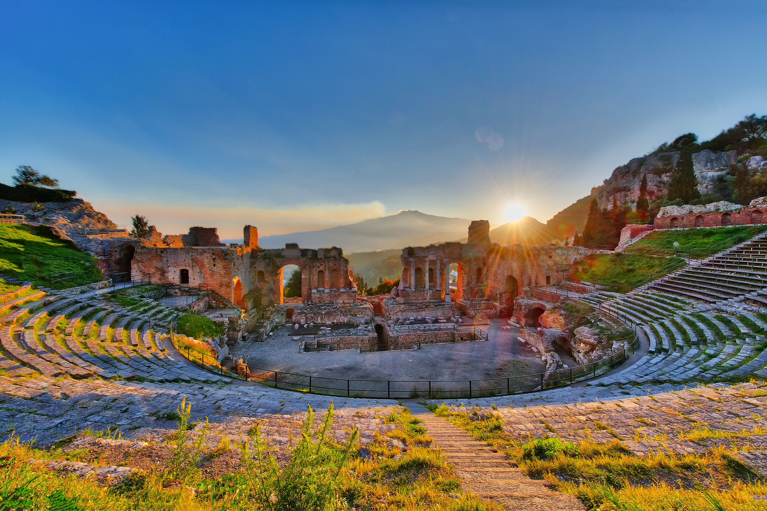 Antikes Amphitheater bei Sonnenuntergang mit Berg im Hintergrund.