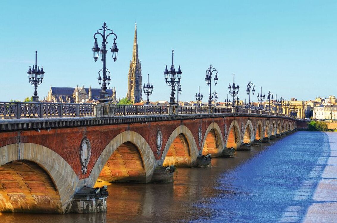 Steinbrücke mit Bögen und Laternen über einem Fluss bei Sonnenschein.